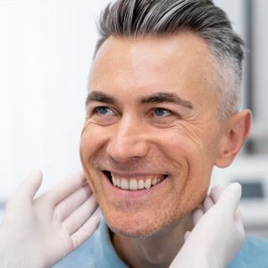 Smiling man during dental implant consultation with dentist examining teeth for tooth replacement