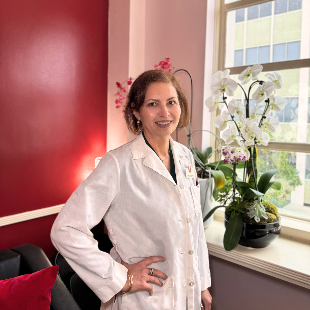Dr. Arminé Nazarian - A Cosmetic and restorative dentist in a welcoming clinic environment standing by the window with floral décor in background of seating area.